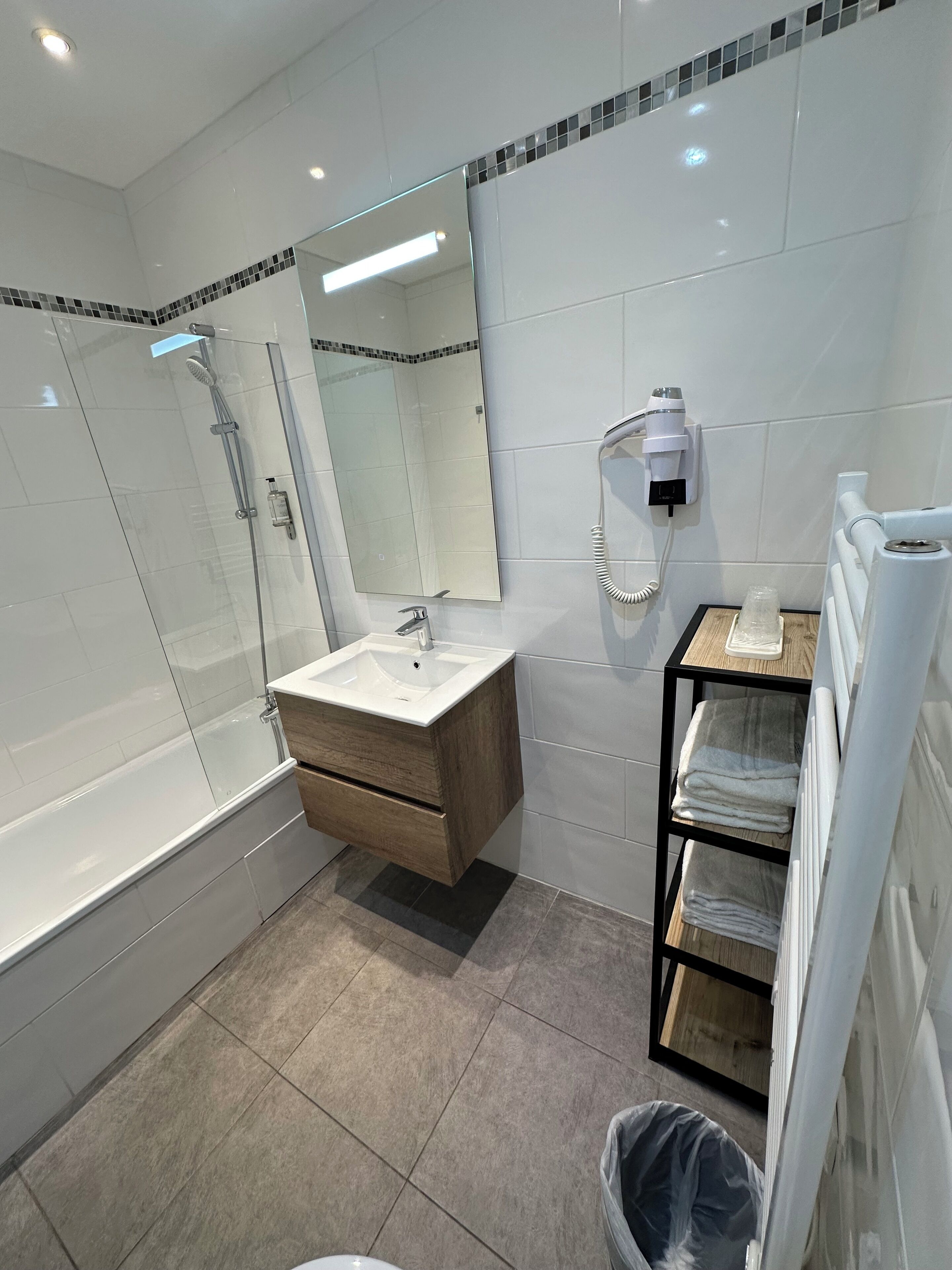 A modern bathroom with a glass-enclosed shower, a wooden vanity with a sink, and a towel rack.