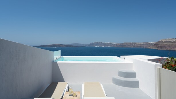 Une terrasse extérieure moderne avec une piscine, des murs blancs et une vue sur la mer et les falaises.