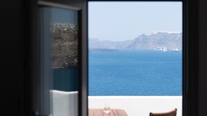 Une vue depuis une pièce avec une fenêtre donnant sur une étendue d’eau, une côte montagneuse et une petite table avec un verre.