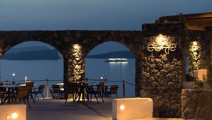 Un arc en pierre mène à une terrasse agrémentée de tables et de chaises, d’où l’on peut admirer un plan d’eau paisible.