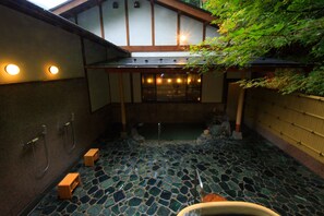 Un onsen japonès tradicional amb un sòl de mosaic de pedra, bigues de fusta i vistes a la natura circumdant.