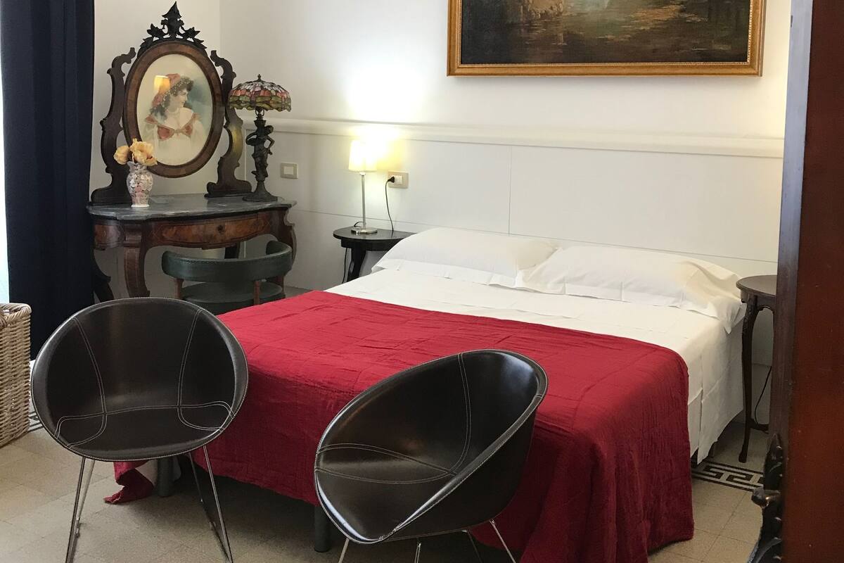 Une chambre d’hôtel avec un lit, deux chaises, une commode, une lampe et un tableau au mur.
