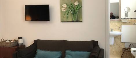 A living room with a sofa, a flat-screen TV, and a painting of flowers.