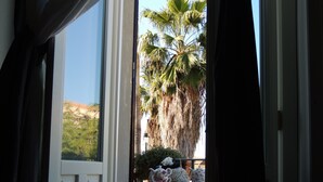 A view through an open door to a balcony with a table set with teapots and cups, palm trees, and a mountainous landscape. - B&B Nike (Syracuse)