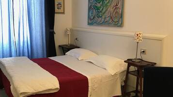 A neatly made bed with a red and white bedspread, a bedside table with a lamp, and a colorful abstract painting on the wall.