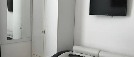 A bedroom with a bed, a white wardrobe, a television on the wall, and a black and white sofa.