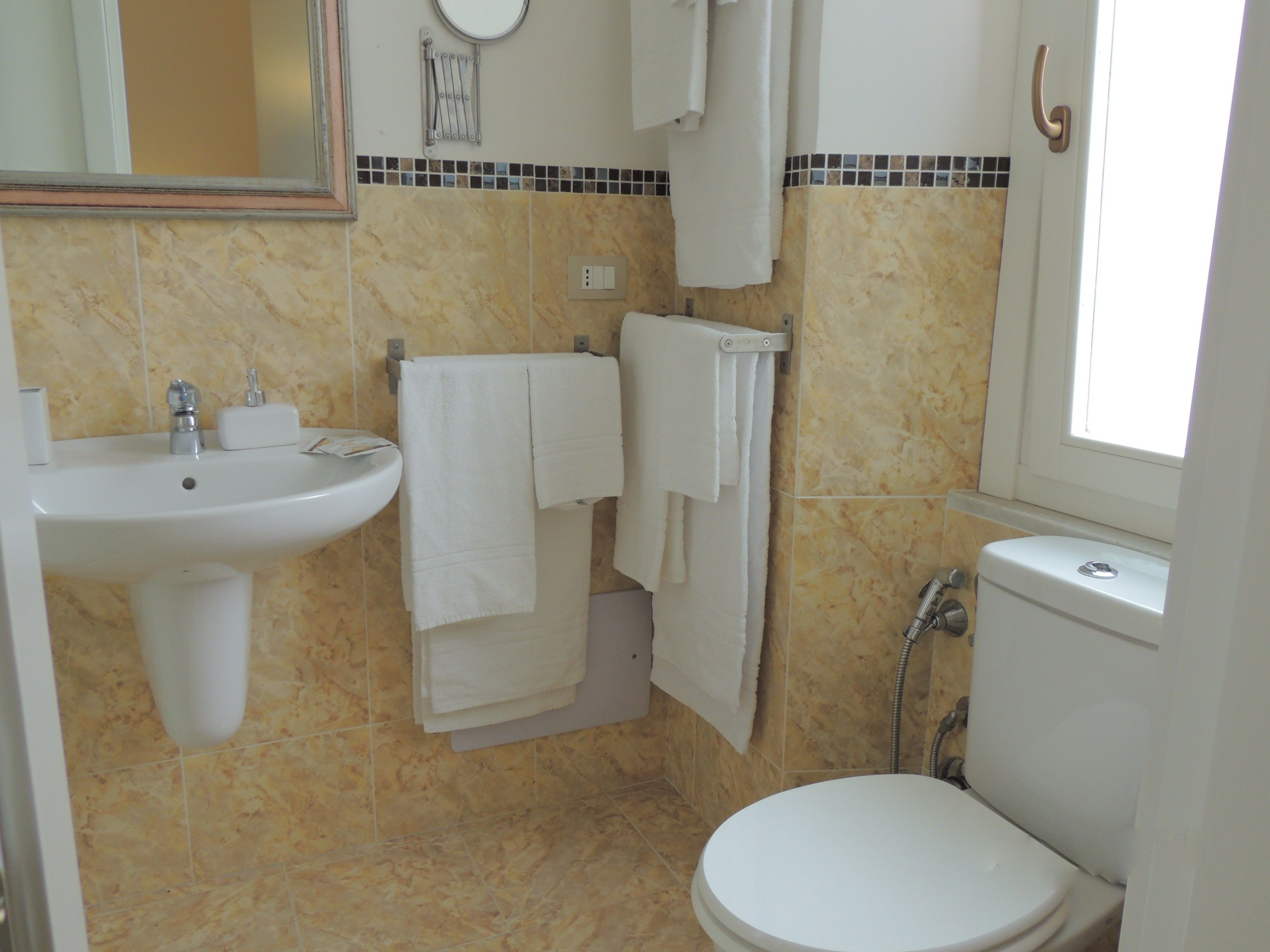 A bathroom with a sink, mirror, towel rack, toilet, and a window.
