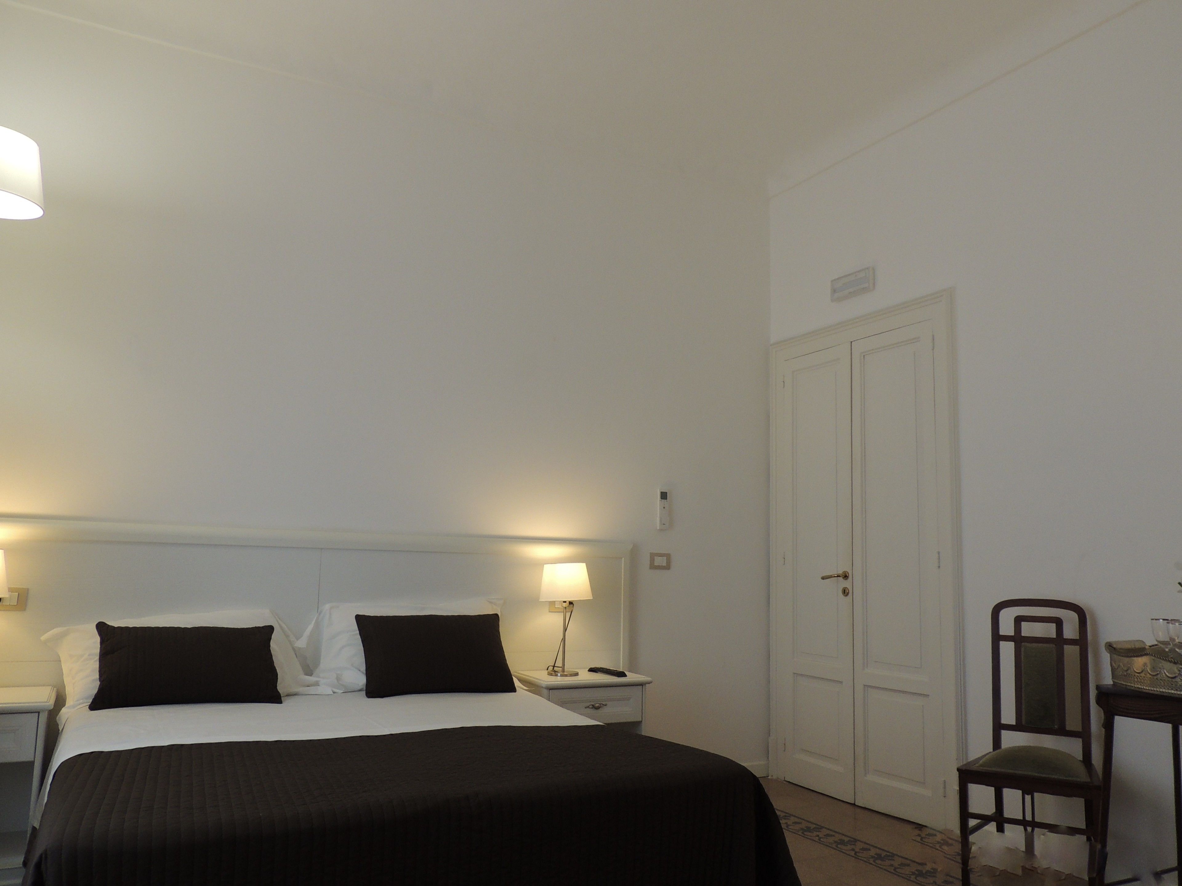 A hotel room with a bed, bedside tables, a nightstand, a lamp, a chair, and a door.