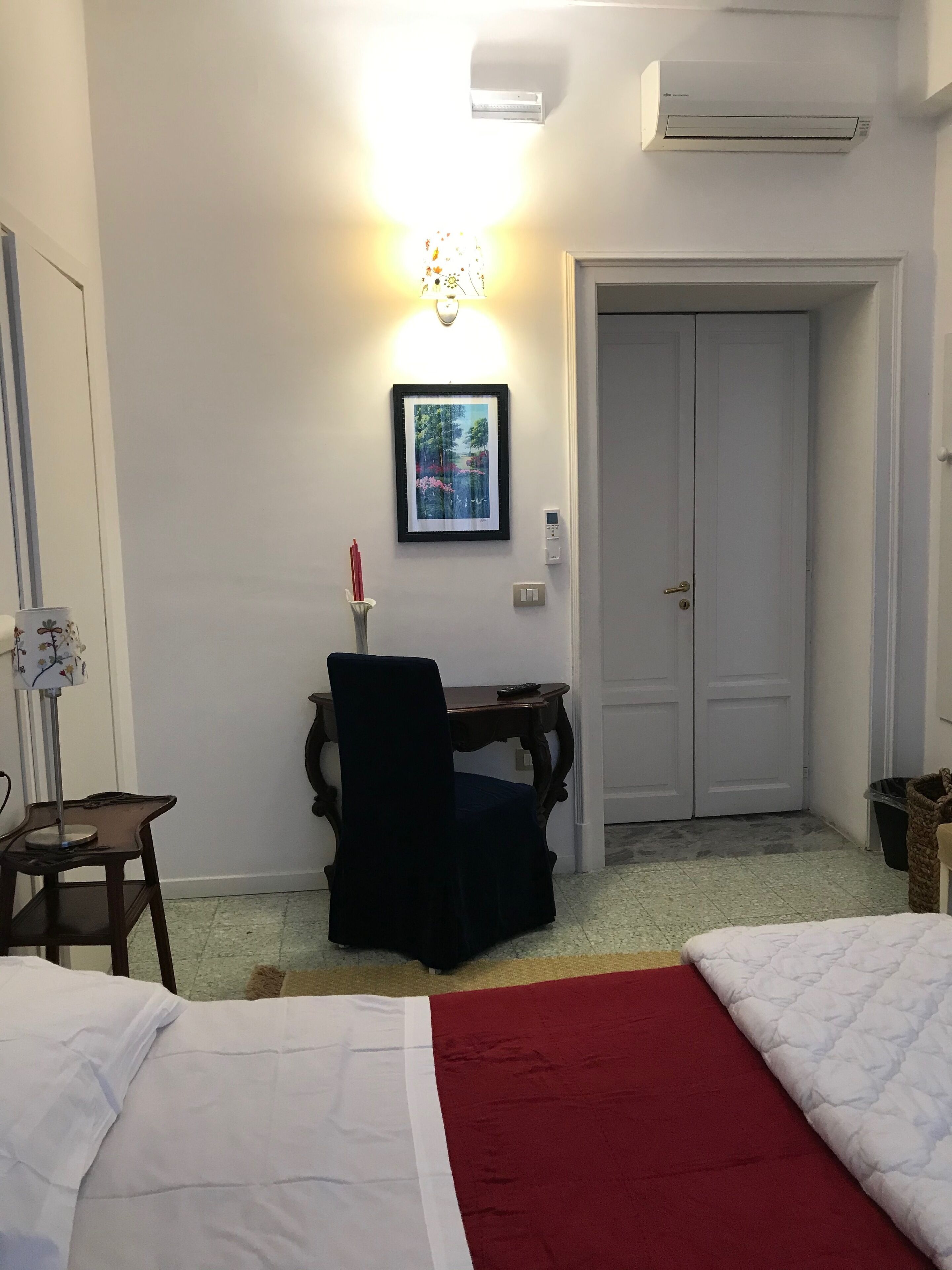 Een slaapkamer met een bed, een bureau met stoel, een ingelijst schilderij aan de muur en een deur.