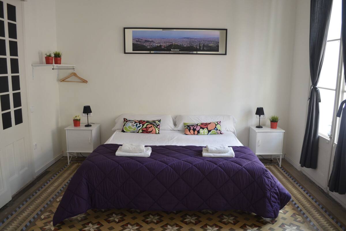A neatly arranged bedroom with a large bed, two bedside tables, a wall-mounted TV, and a patterned floor.