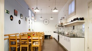 A modern dining area with wooden tables and chairs, a kitchen with white cabinets, and pendant lighting. - 360 Hostel Borne (Barcelona)