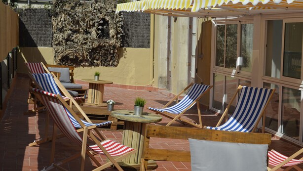 A patio area with striped lounge chairs, a small table with a plant, and a yellow awning. - 360 Hostel Borne (Barcelona)