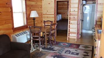 Interior acogedor de una cabaña con comedor, un sofá, un tapete estampado y una escalera que lleva a un dormitorio.