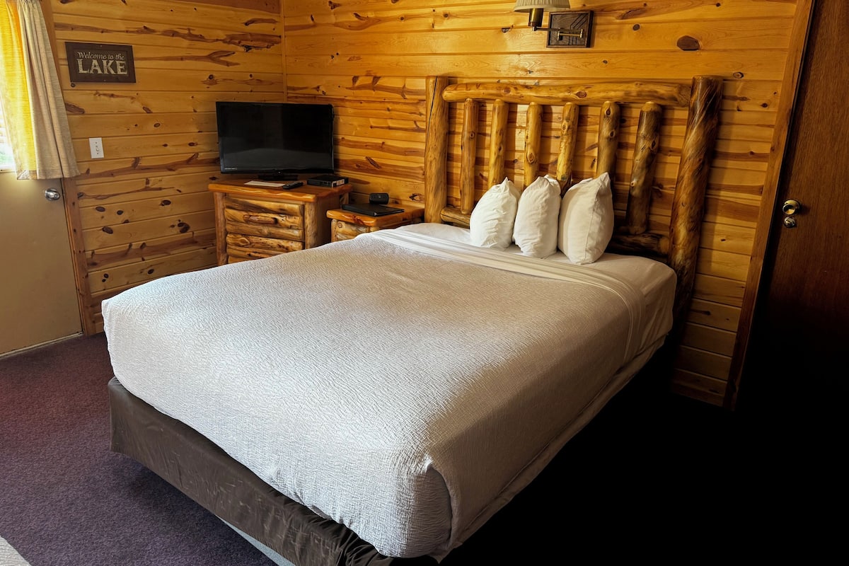 Une cabane en bois comprenant un lit, un téléviseur et une pancarte sur laquelle on peut lire : « Bienvenue au bord du LAC ».