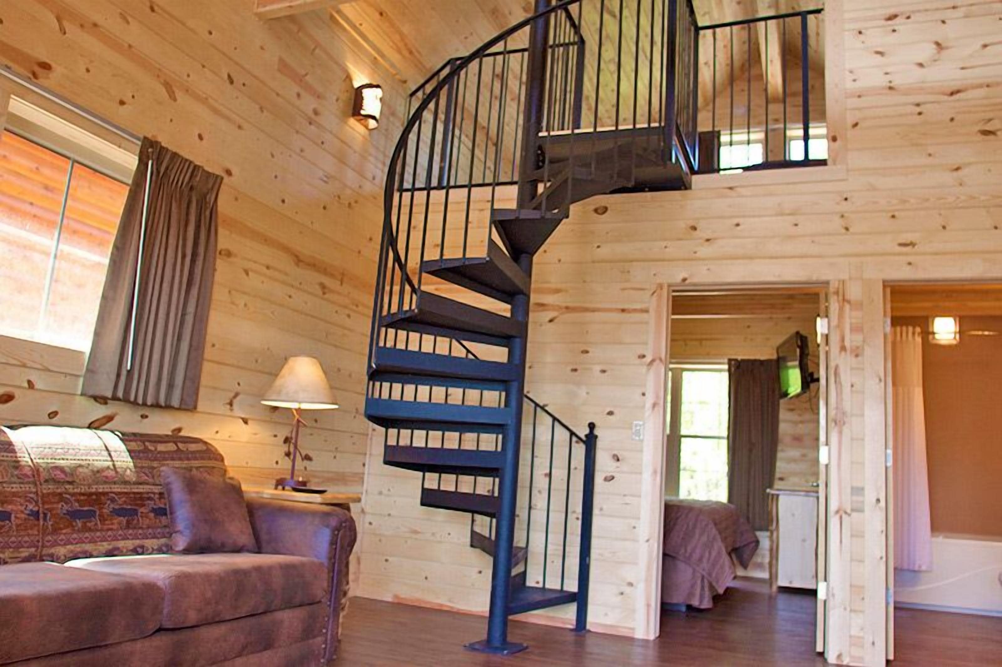 A wooden cabin interior with a spiral staircase, a sofa, and a television.