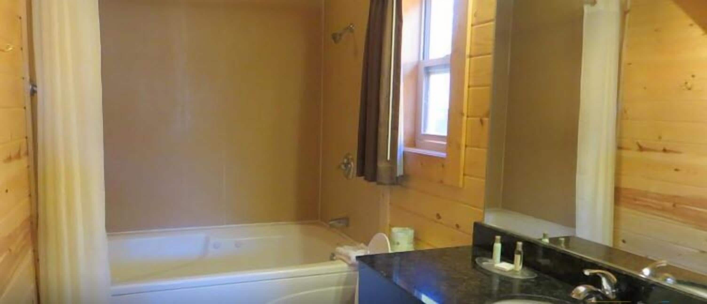 Un baño con revestimiento de madera que incluye una bañera, un lavamanos con artículos de aseo y un espejo.