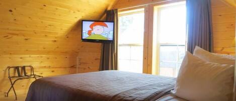 Ein Zimmer in einer Holzhütte mit einem Bett, einem Fernseher an der Wand und einem Fenster.