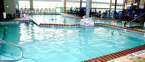 An indoor swimming pool with clear water, a central fountain, and a tiled deck surrounding the pool.