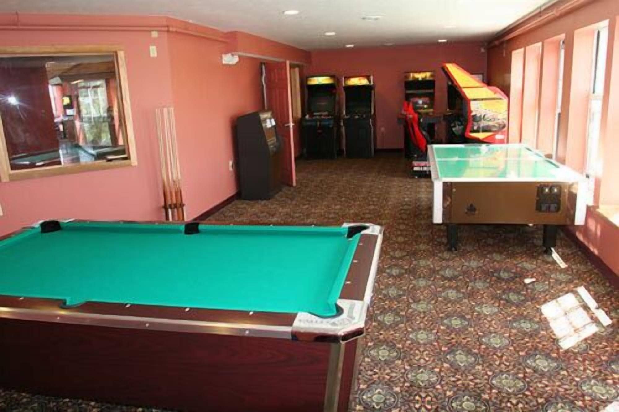 A pool table in a room with arcade games and a billiards table.