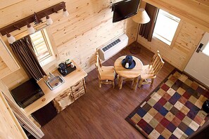 Een compact houten vakantiehuisje met een keukenhoek, een eettafel en een aan de muur bevestigde televisie.