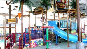 Een overdekt waterpark met glijbanen, klimconstructies en een piratenthema bord.