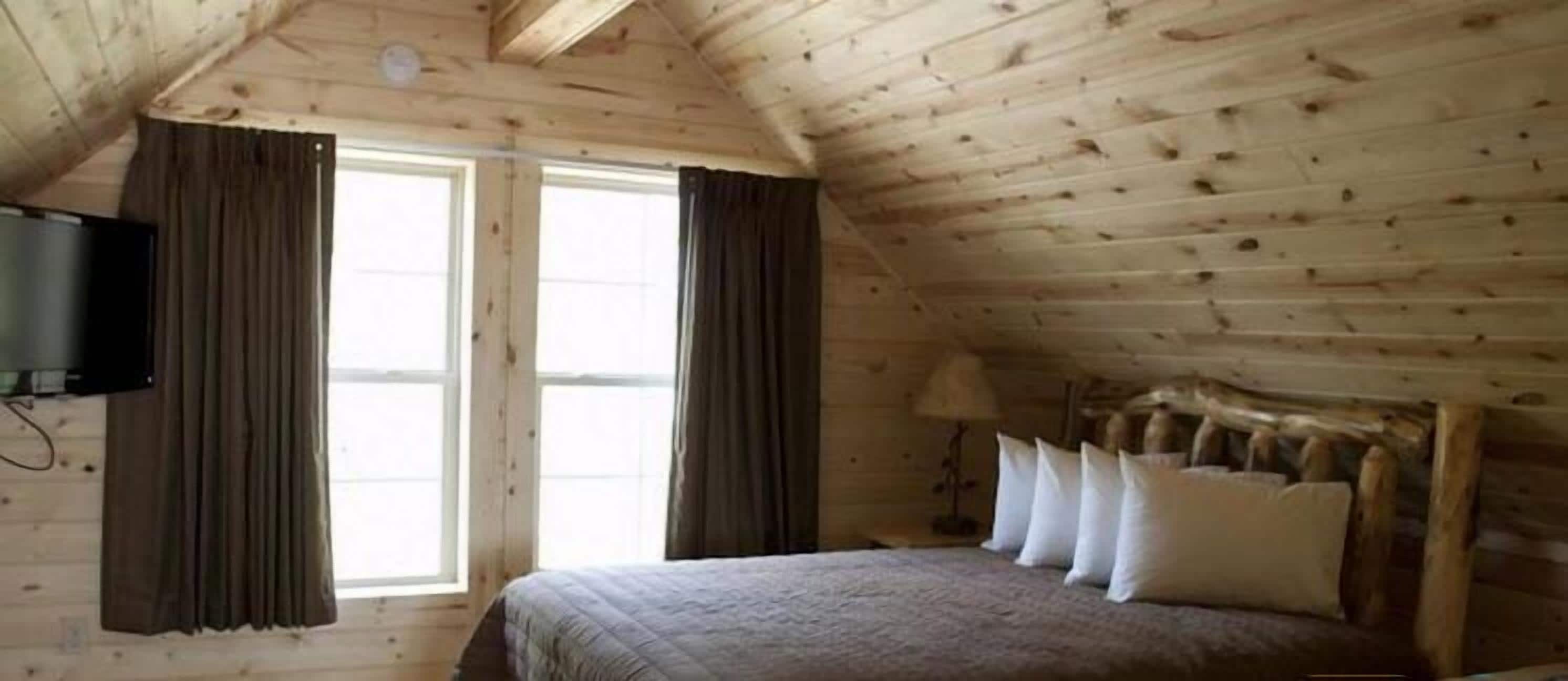 Una habitación de madera con cama, cortinas, televisor y lámpara.