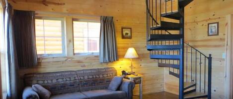 A log cabin interior with a stone-patterned sofa, a lamp, a staircase, and wooden walls.