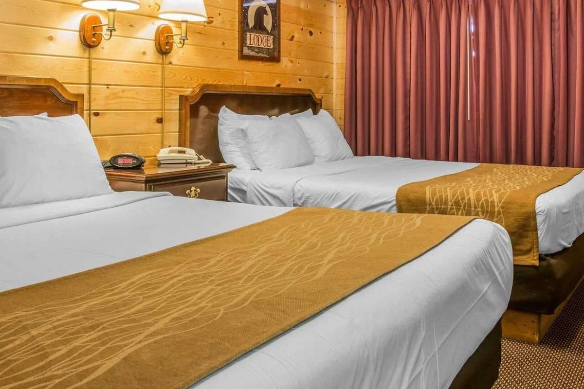 Une chambre d’hôtel avec deux lits, des murs en bois, une tête de lit en bois, une table de chevet avec un téléphone et un panneau accroché au mur.