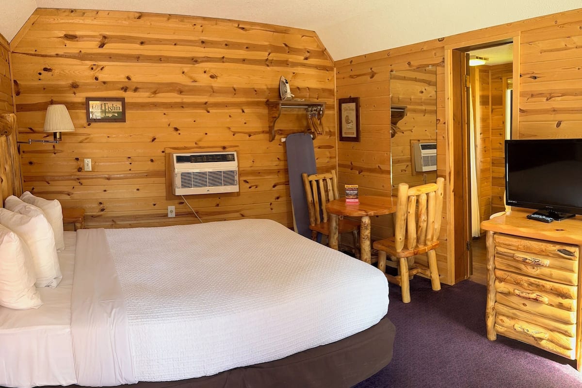 Une chambre dans un chalet en bois, comprenant un lit, un bureau, une chaise, une télévision et une petite table.