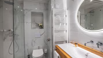 Un baño moderno con ducha de vidrio, inodoro blanco, tocador con espejo y perchero para toallas.