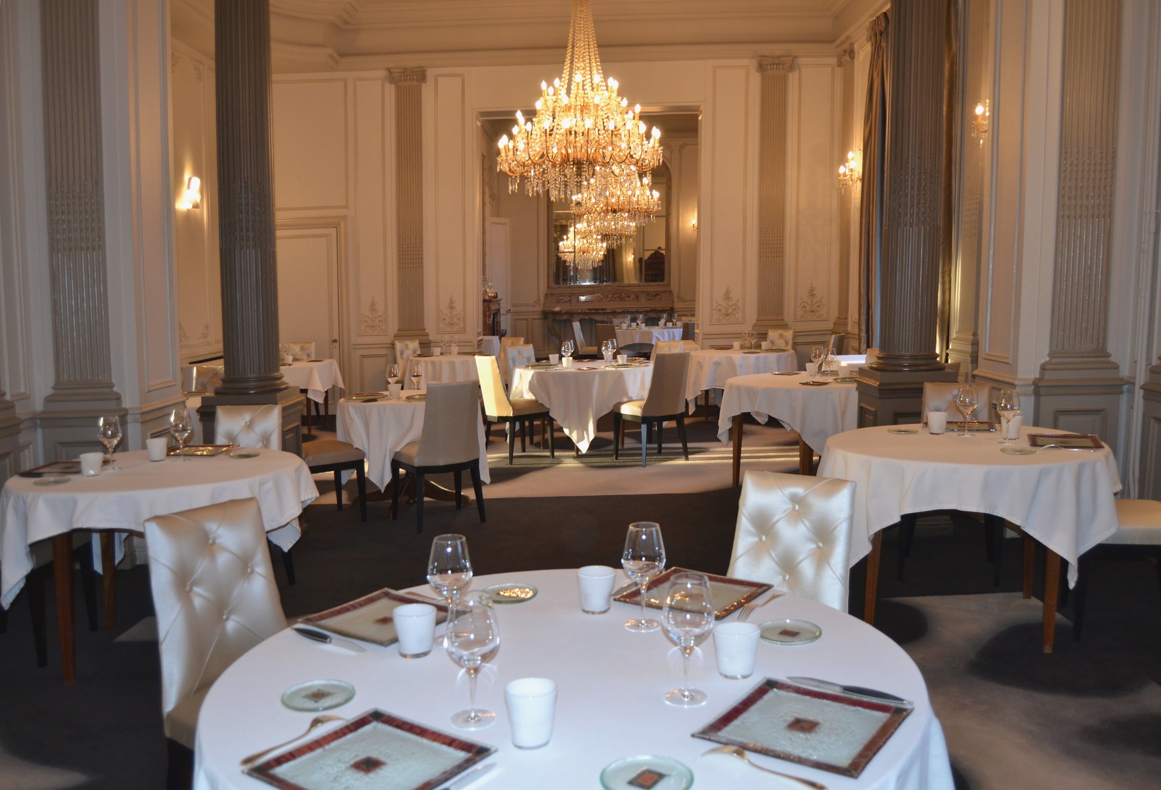 A formal dining room with round tables, white tablecloths, and elegant chairs.