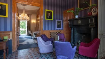 A room with a patterned floor, wooden furniture, a fireplace, and framed portraits on the wall.