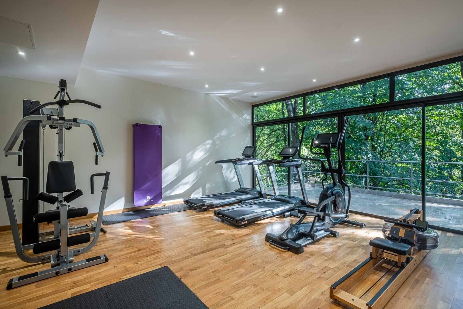 A modern gym with cardio machines, a weight bench, and a yoga mat.