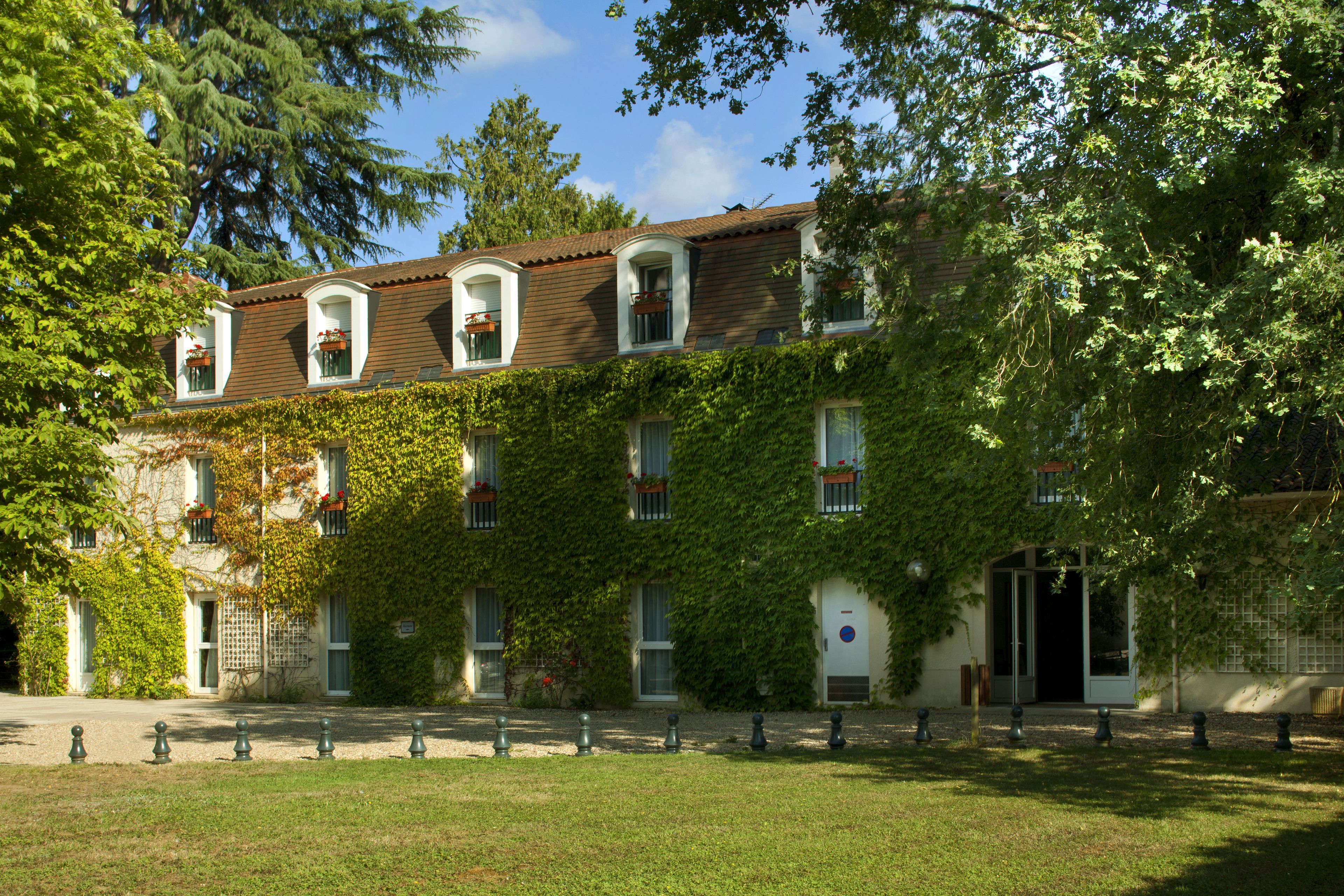 Un edificio con uno stile architettonico tradizionale, caratterizzato da una facciata simmetrica, diverse finestre con persiane e un ingresso coperto.