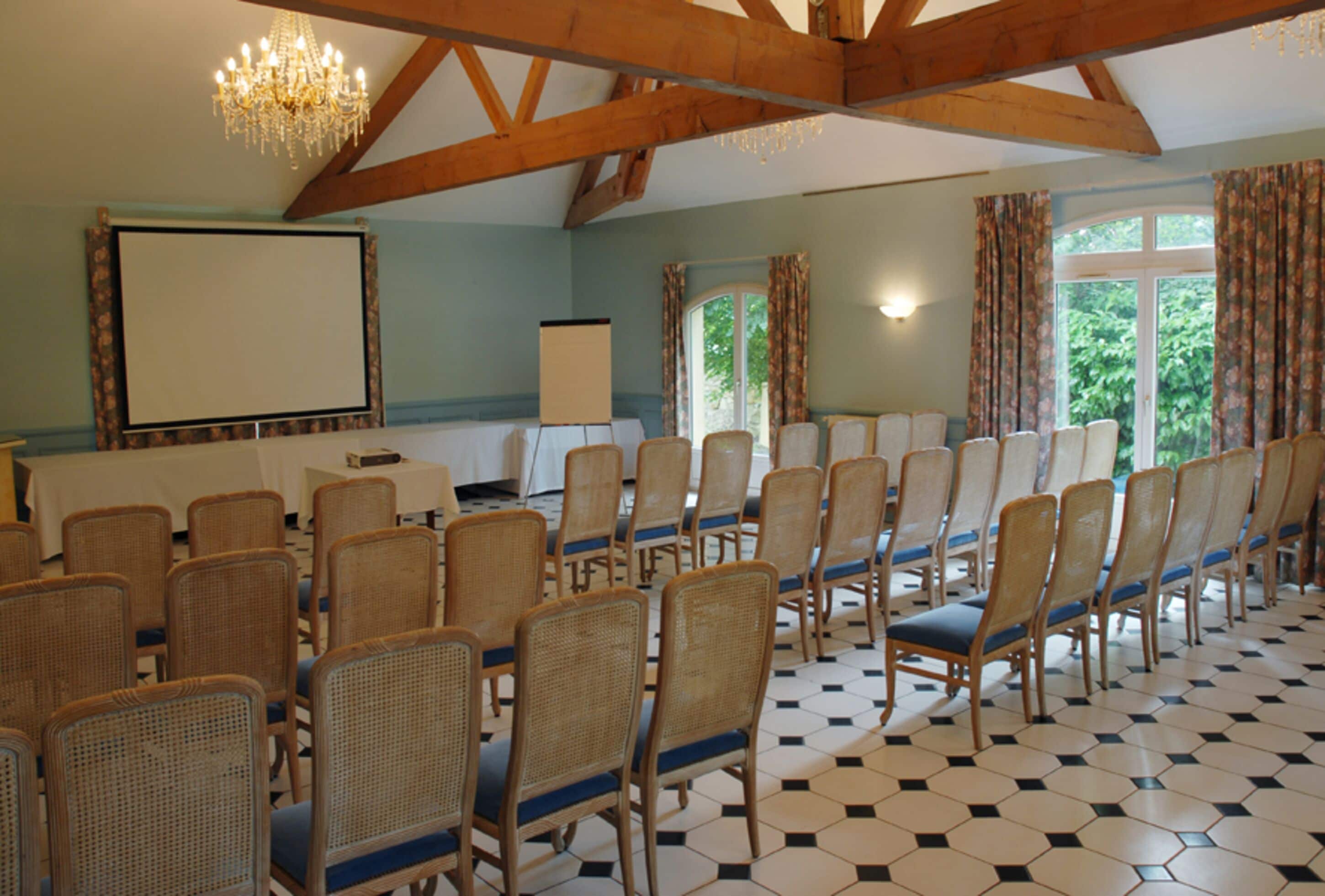 A conference room with rows of wicker chairs, a projector screen, and a chandelier.