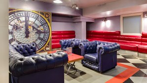 A room with red and blue leather seating, a large wall clock, and a checkered floor. - Clink 261 Hostel (London)