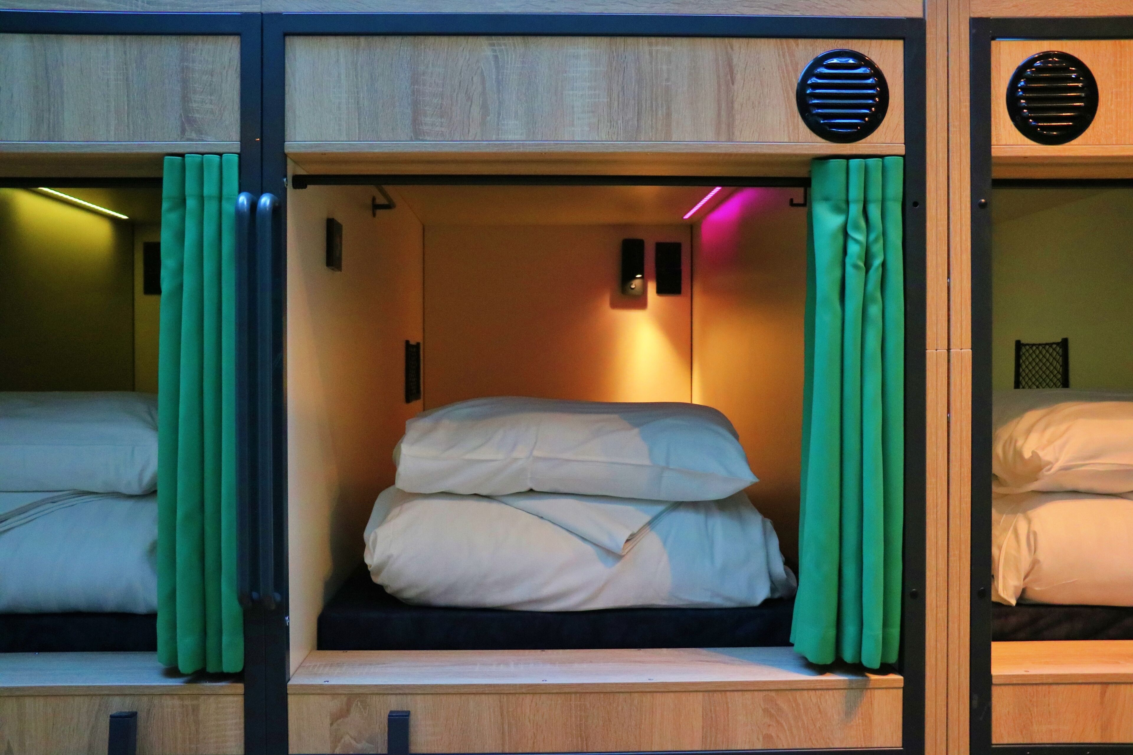 A compact hotel room with two beds, each with a wooden headboard and a green curtain.