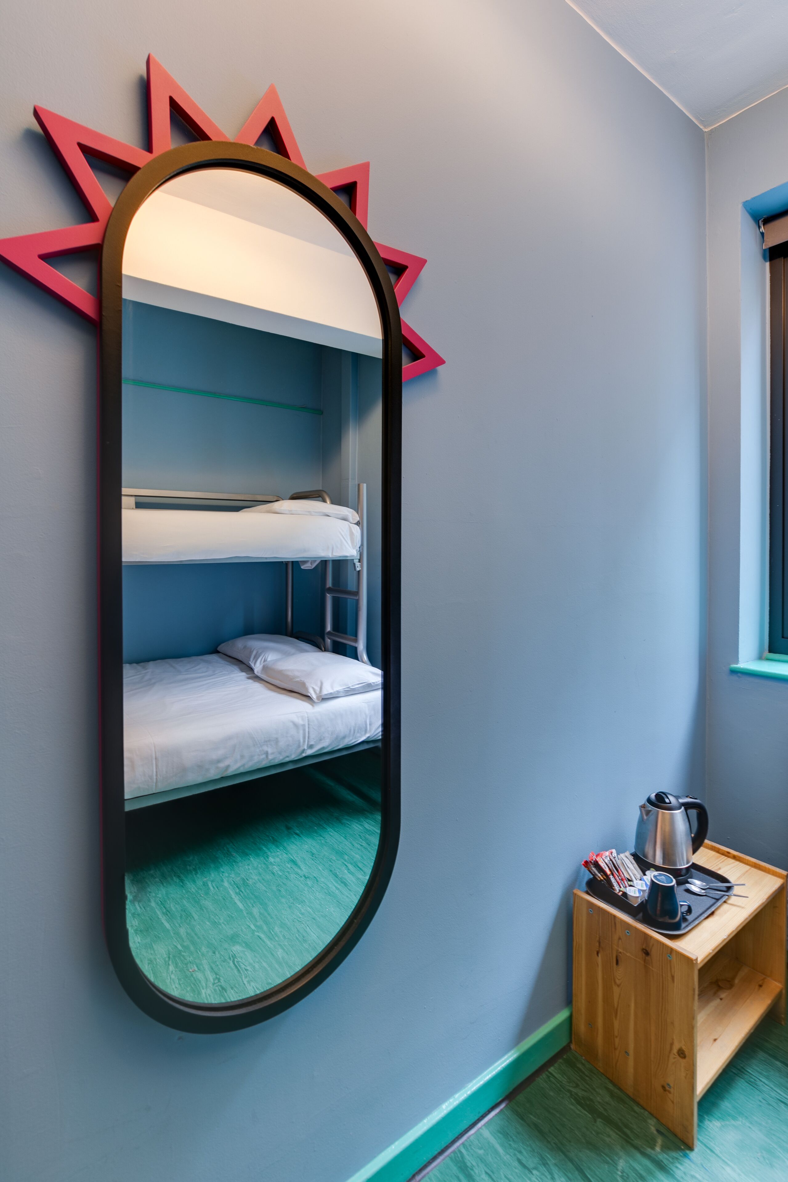 A bunk bed with a mirror, a wooden side table with a kettle, and a star-shaped decoration on the wall.