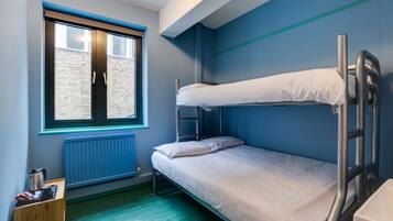 A bunk bed room with a window, radiator, and a small wooden cabinet with items on it.
