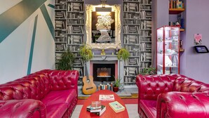 A living room with red leather sofas, a fireplace, a bookshelf, and a guitar. - Clink 261 Hostel (London)