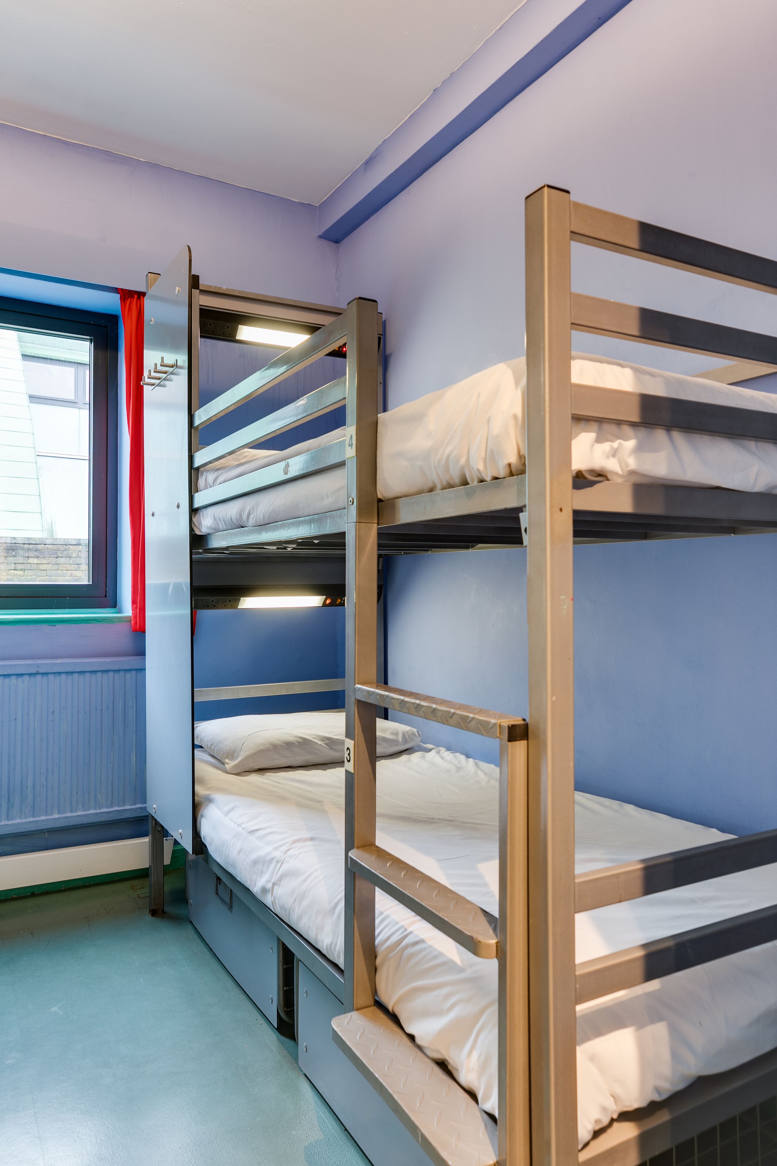A bunk bed room with a window and red curtain.