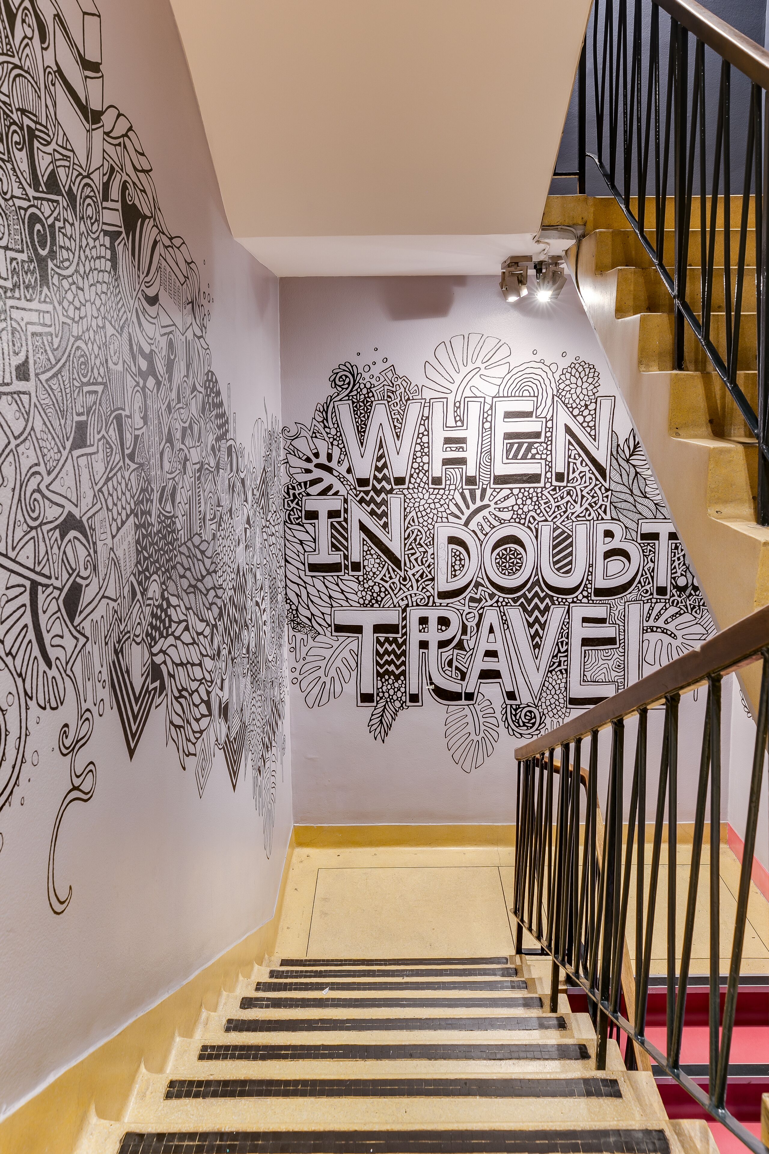 A staircase with a wall mural featuring intricate black and white patterns and the text "WHEN IN DOUBT TRAVEL".