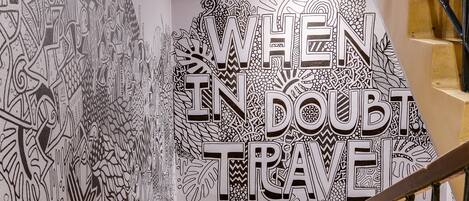 A staircase with a wall mural featuring intricate black and white patterns and the text "WHEN IN DOUBT TRAVEL".