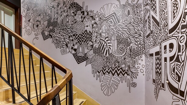 A staircase with a wooden handrail and a wall with intricate black and white patterns. - Clink 261 Hostel (London)