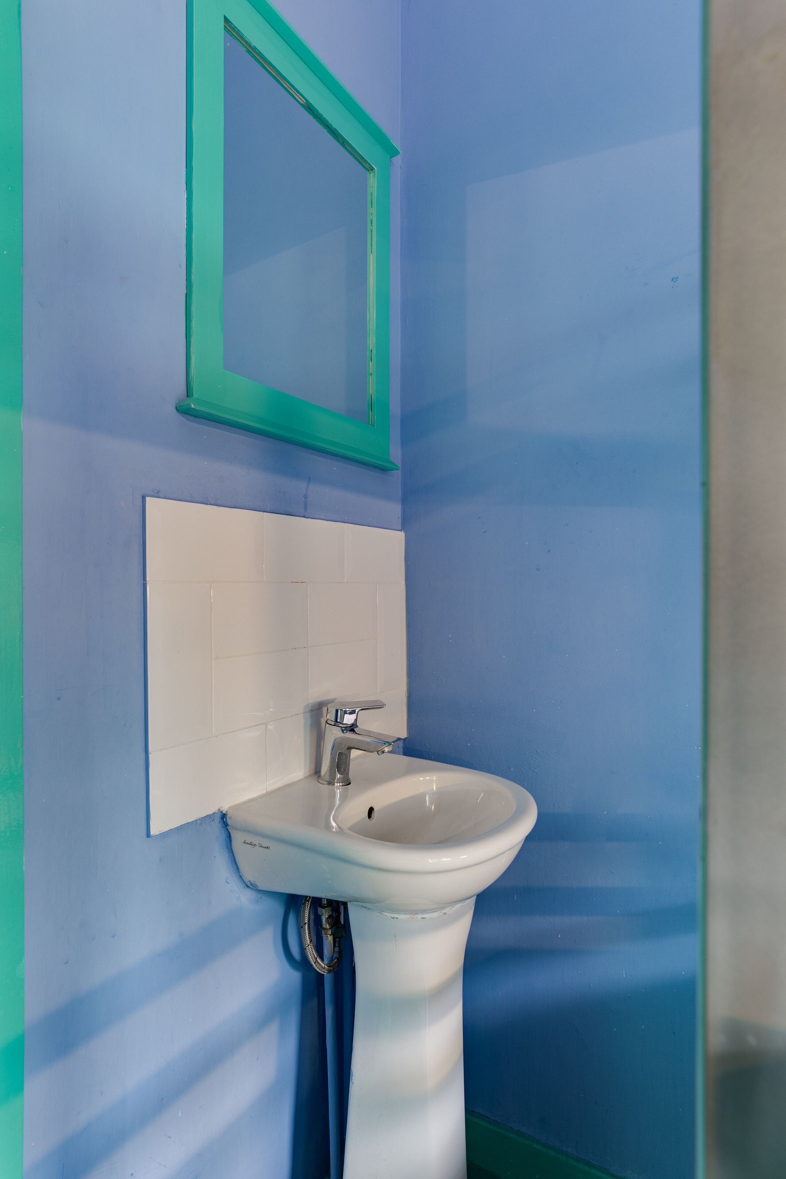 A bathroom with a white sink, a blue wall, and a green-framed mirror.