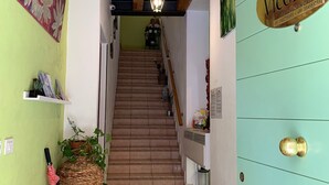 A hallway with a staircase leading to a room, a door with a sign, and a red umbrella on a stand. - Vicolo 22 (Verona)