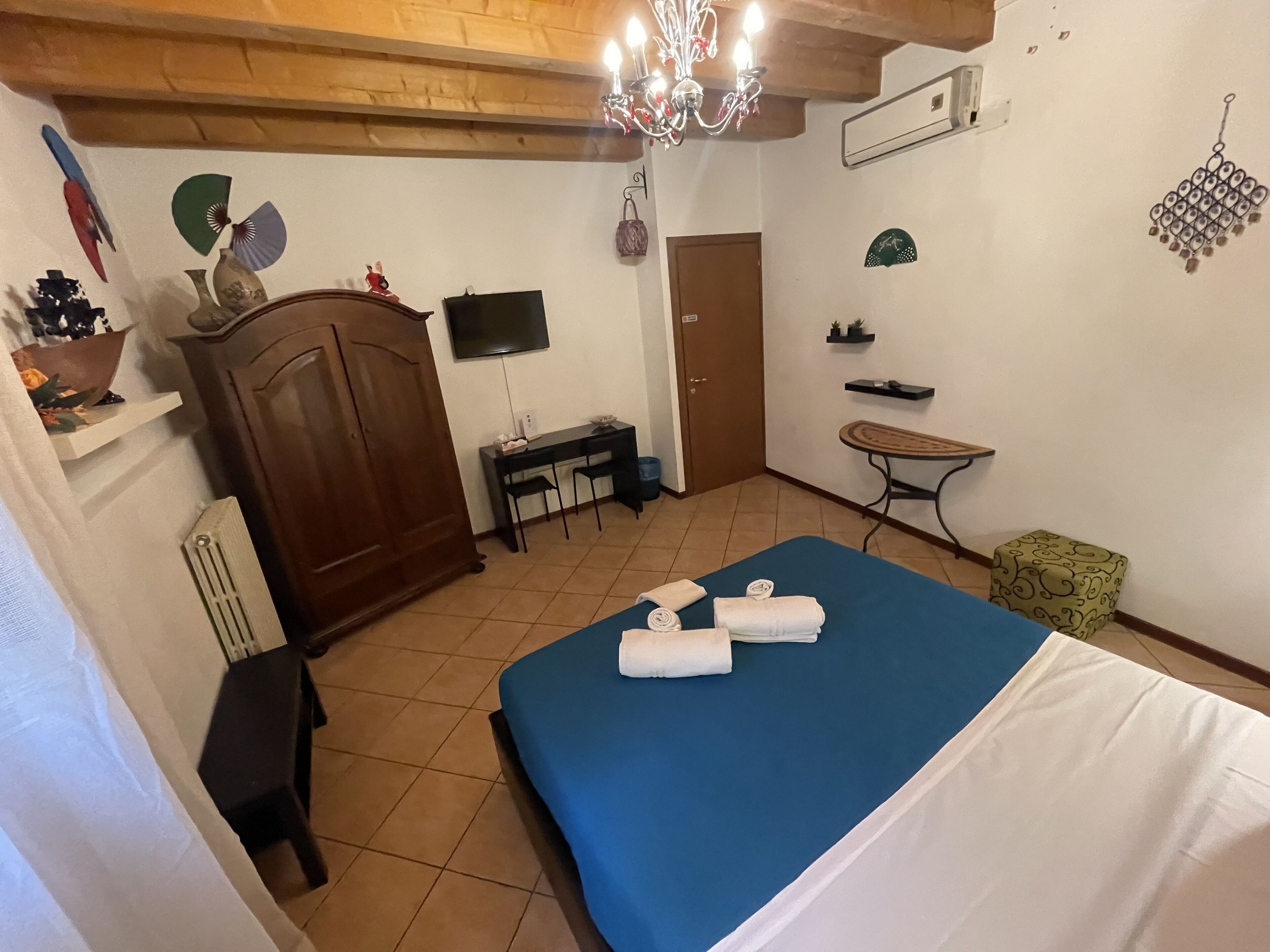 A hotel room with a bed, a desk, a chair, a wardrobe, a TV, and a small table with a chair.