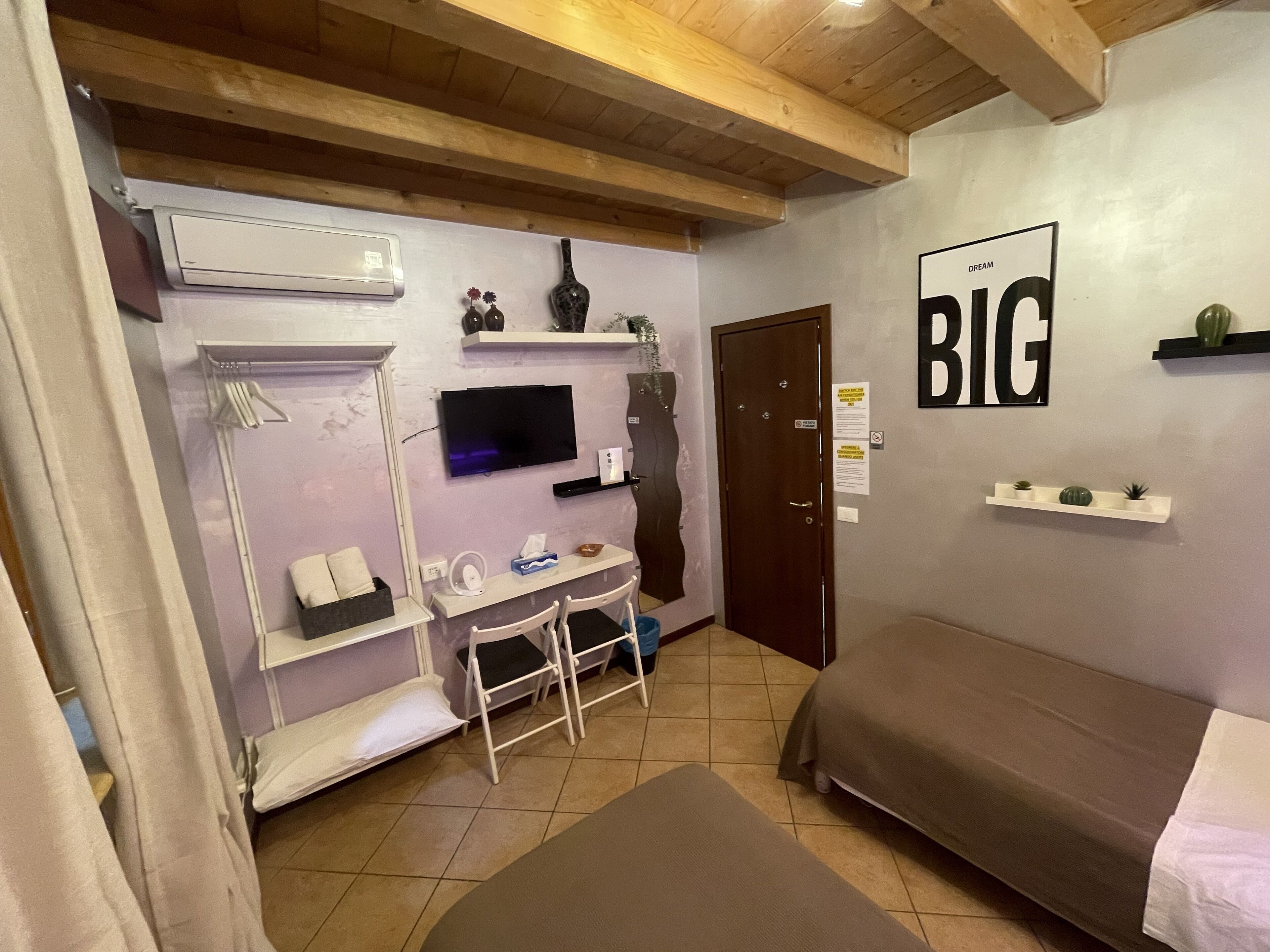 Una habitación pequeña con cama, escritorio, silla, televisión y puerta.