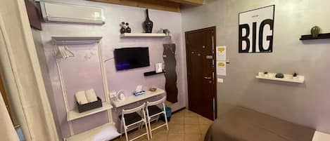 Una habitación pequeña con cama, escritorio, silla, televisión y puerta.