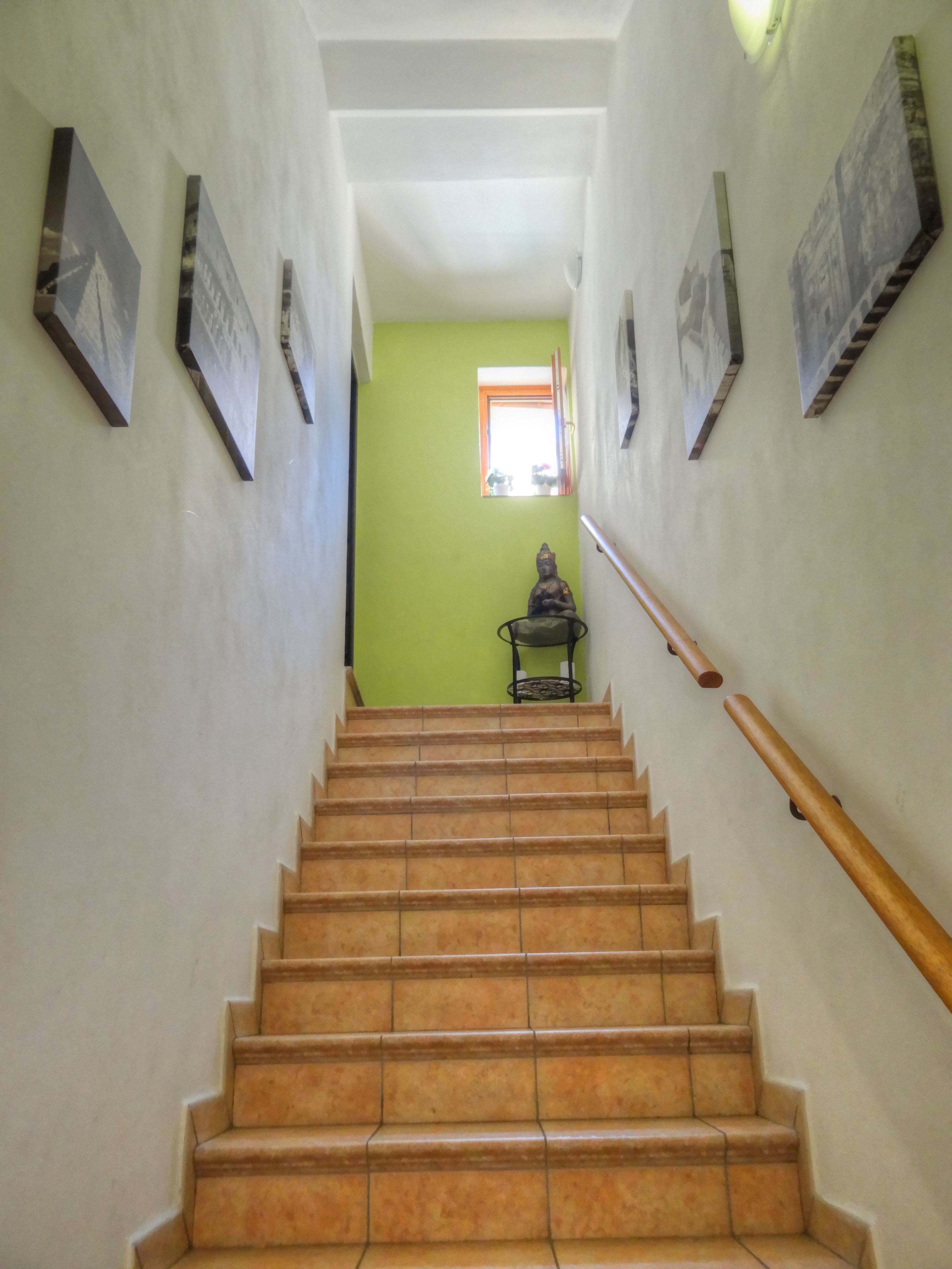 A staircase with a handrail, leading to a room with green walls and a small statue.